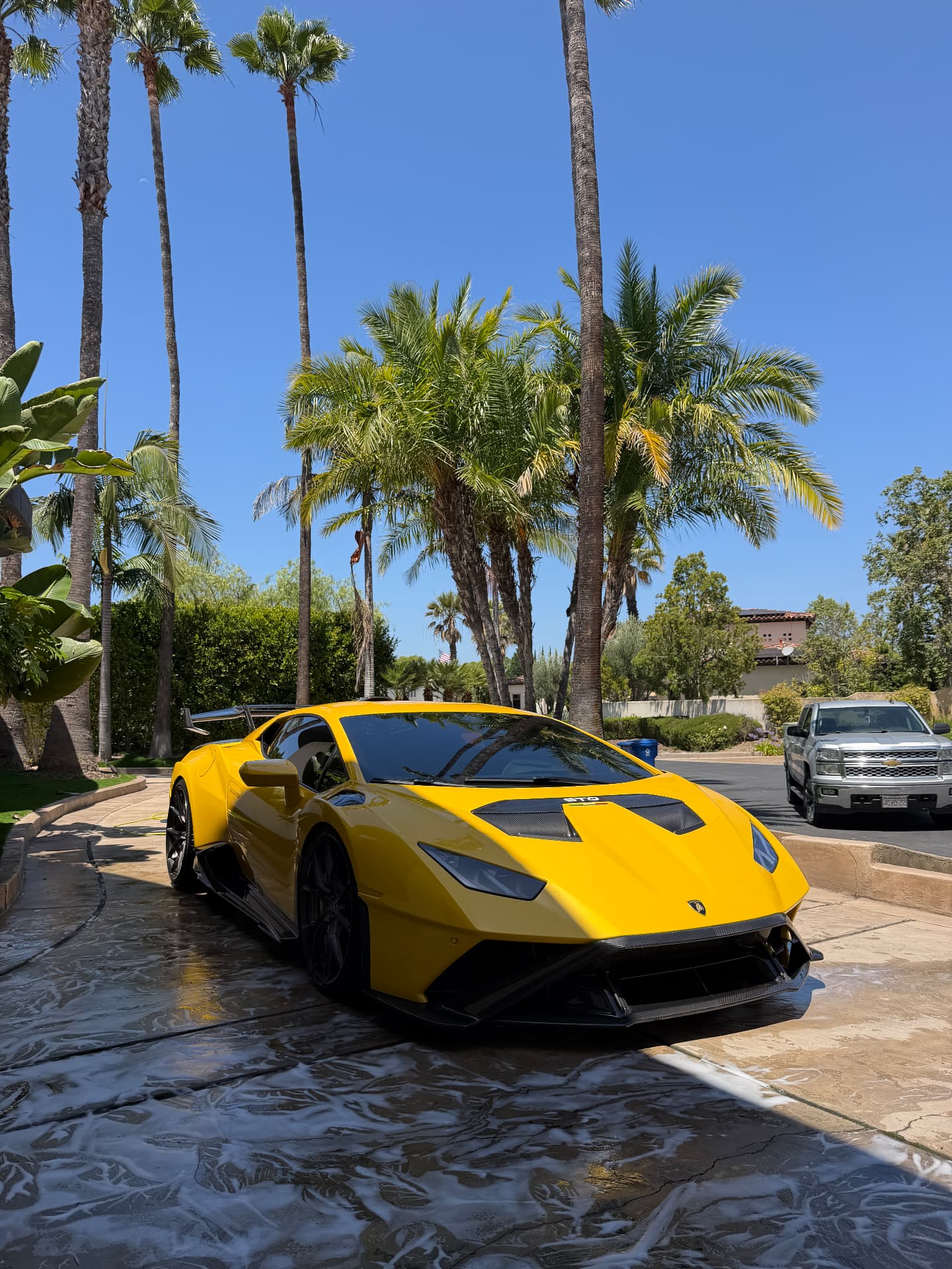 Yellow Lamborghini detailed on a stone driveway with palm trees