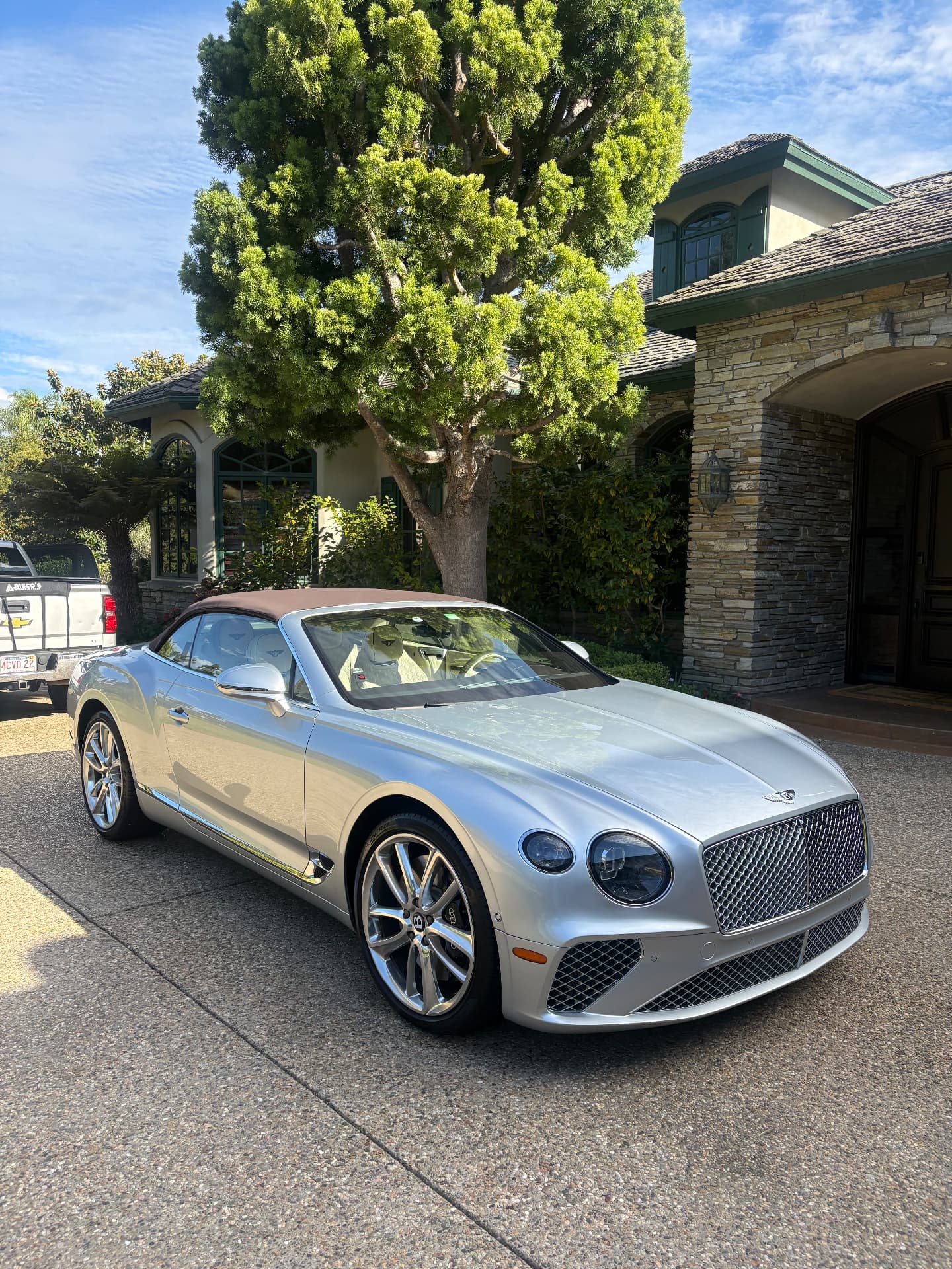 Silver Bentley convertible with a tan soft top parked in a residential driveway